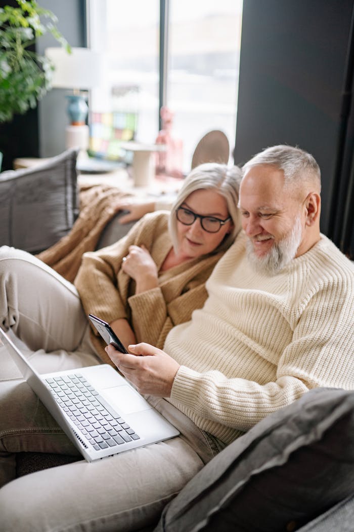 Senior couple enjoying togetherness using laptop and smartphone on a sofa at home.