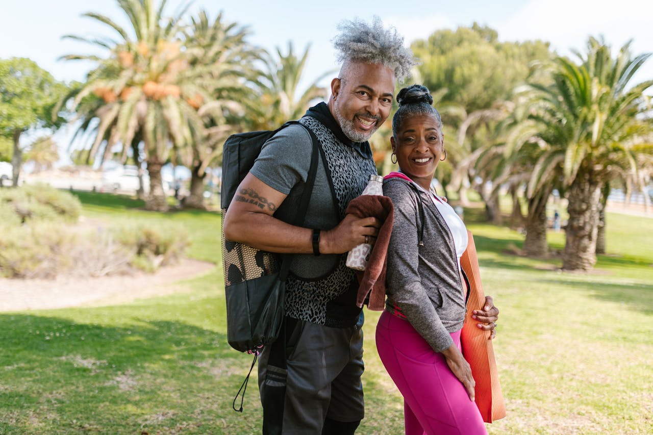 Happy senior couple practicing yoga outdoors in a park setting, promoting wellness and togetherness.